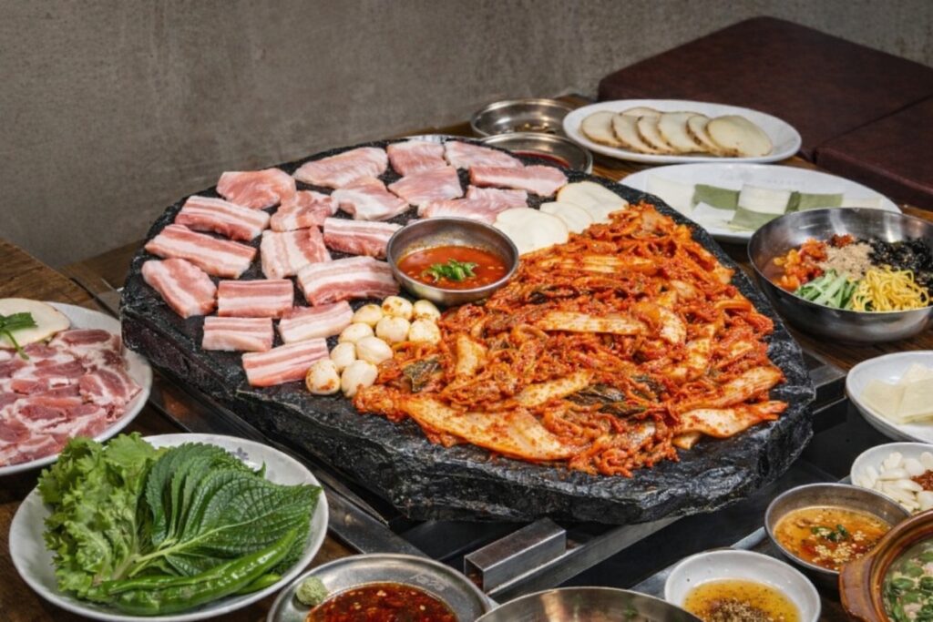 Stone grill Korean BBQ in Jongno with pork belly, kimchi, garlic, and side dishes cooking together on a sizzling hot plate