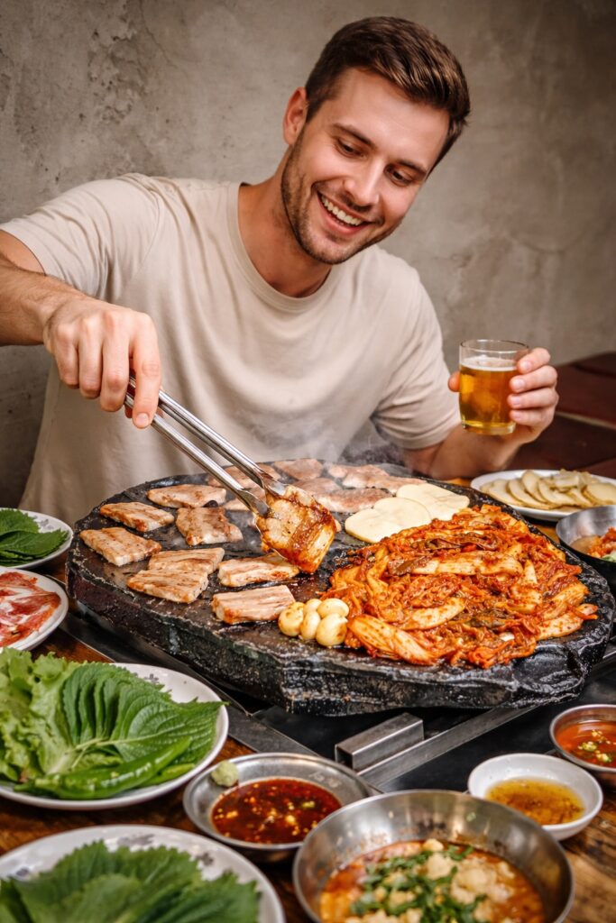 Korean BBQ experience in Jongno with a traveler grilling samgyeopsal on a hot stone grill and enjoying beer at a local restaurant