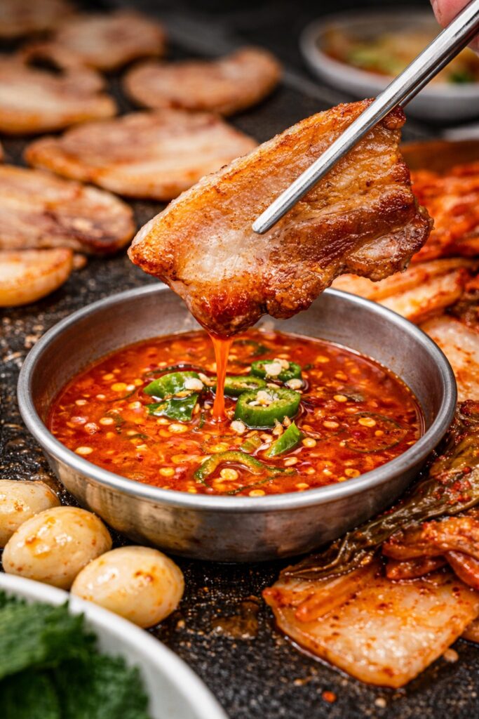 Crispy grilled samgyeopsal dipped in spicy Korean sauce showing juicy texture and rich flavor close up