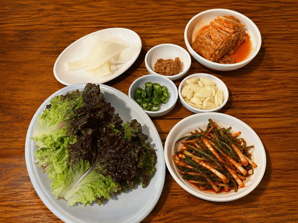 Korean BBQ side dishes including kimchi garlic lettuce and green onion salad at Daeha Sikdang