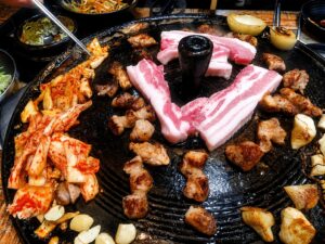Traditional Korean pork belly BBQ grilling on an iron lid grill with kimchi and garlic in Seoul
