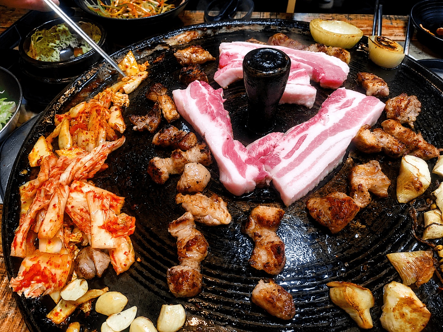 Traditional Korean pork belly BBQ grilling on an iron lid grill with kimchi and garlic in Seoul
