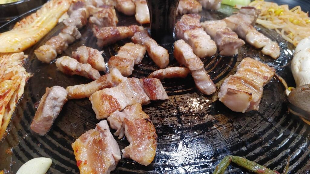 Close-up of crispy grilled Korean pork belly cooking on a traditional iron grill