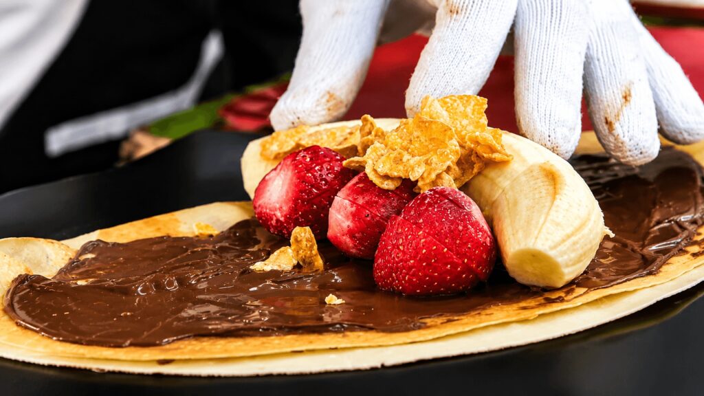 Nutella crepe with fresh strawberries and banana being prepared at a Seoul street food stand