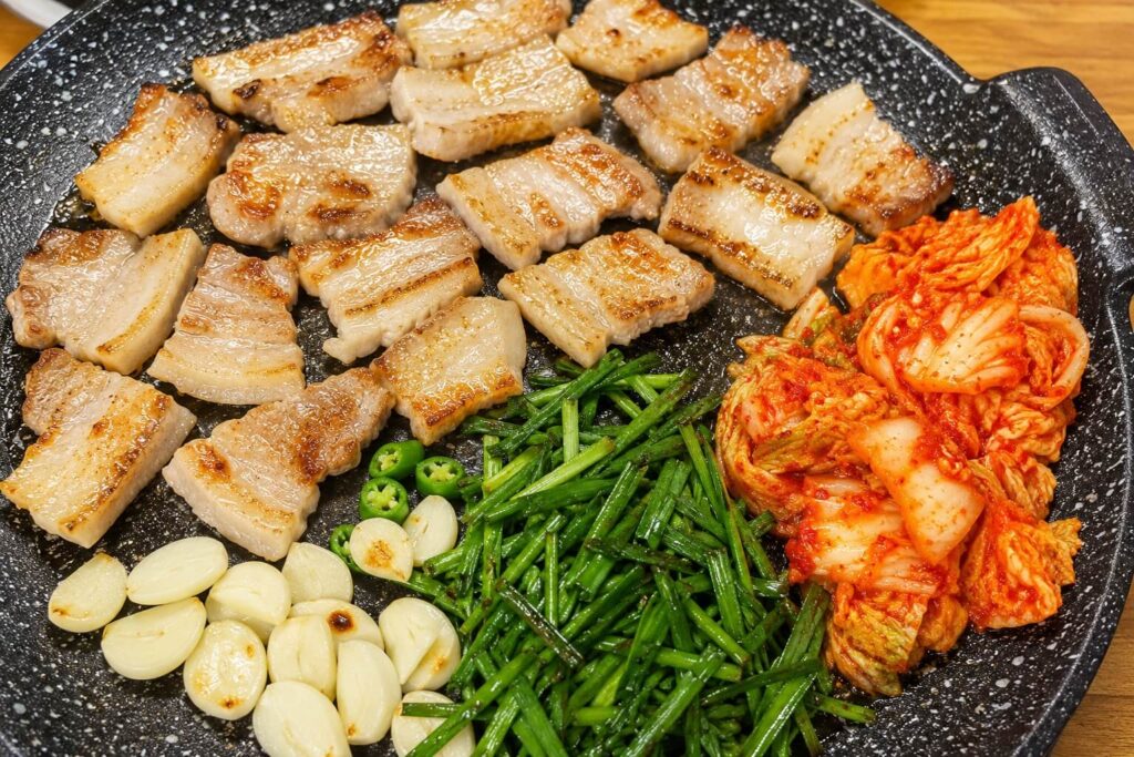 Perfectly grilled Korean pork belly served with kimchi, garlic, green chili, and chives at Happy Restaurant