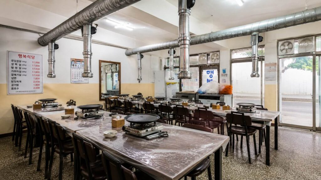 Interior dining area with Korean BBQ tables and exhaust hoods at Happy Restaurant