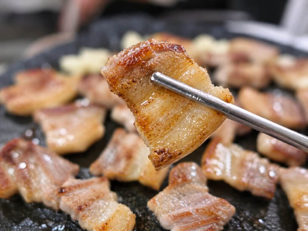 Close-up of juicy grilled Korean pork belly held with metal chopsticks
