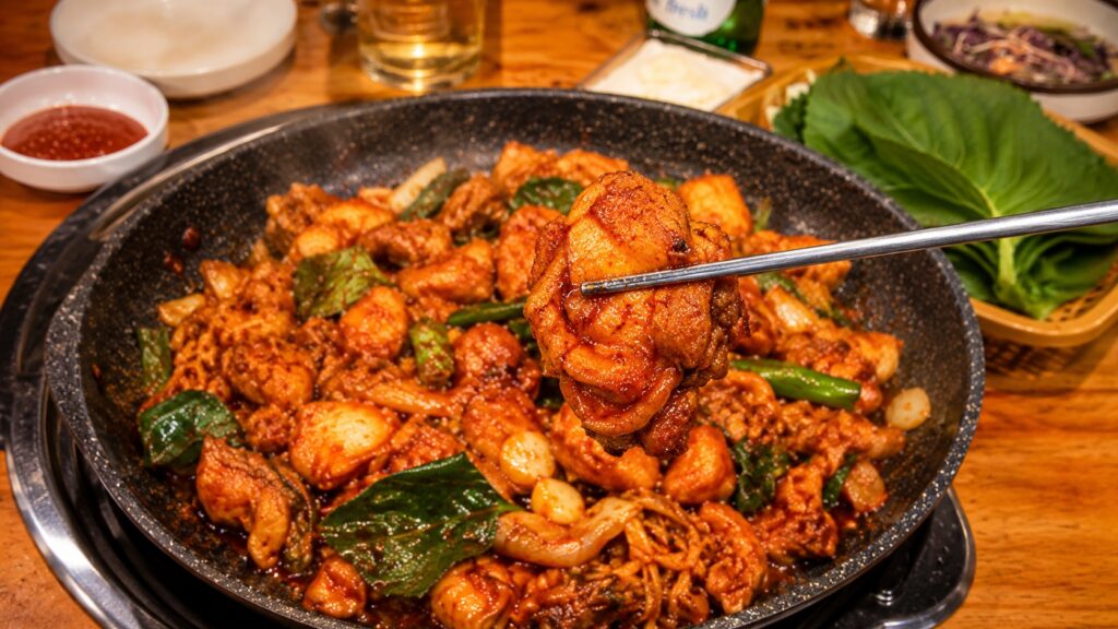 A piece of spicy Korean dakgalbi held with chopsticks at a restaurant near Seongsu