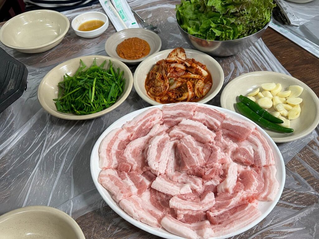 Fresh pork belly platter with lettuce, kimchi, garlic, green chili, and chives ready for Korean BBQ