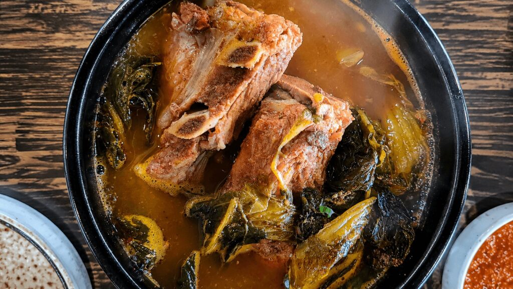 Full bowl of Korean gamjatang with pork backbone and greens in