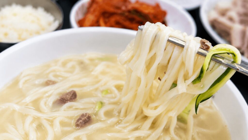 Close-up of handmade kalguksu noodles lifted with chopsticks